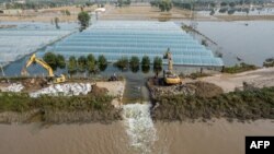 Tim SAR menggali dengan ekskavator untuk membuat saluran guna melepaskan air banjir akibat hujan deras di kota Jinzhong, Jiexiu, provinsi Shanxi utara, China, 11 Oktober 2021. (AFP) 