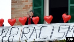 Une femme sur son balcon où elle a mis des ballons rouges portant le nom des victimes et une banderole disant "non au racisme" lors d'une manifestation antiraciste dans la ville de Macerata, en Italie, le 10 février 2018.