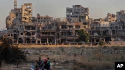 People ride their motorcycle by damaged buildings in the old town of Homs, Syria. (Aug. 15, 2018) 