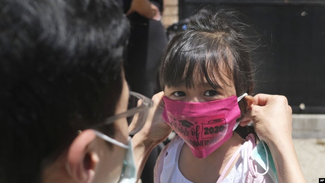 FILE - In this June 10, 2020, file photo, Olivia Chan's father helps her with a new mask she received during a graduation ceremony for her Pre-K class in front of Bradford School in Jersey City, N.J. (AP Photo/Seth Wenig, File)