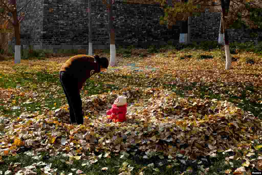 A mother looks at her daughter sitting in a pile of fallen leaves shaped like a heart, in Beijing, China, Nov. 19, 2018.