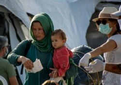 A woman with a baby holds a document before entering the new temporary refugee camp in Kara Tepe, on the northeastern island of Lesbos, Greece, Sept. 18, 2020.