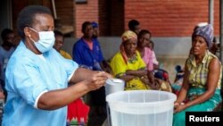 FILE - Violett Motta, a health surveillance assistant in Malawi, mixes chlorine with water to disinfect it at a health center in response to the latest cholera outbreak in Blantyre, Malawi, Nov. 16, 2022. 