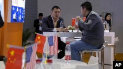 FILE - Visitors chat near American and Chinese flags displayed at a booth for an American company promoting environmental sensors during the China International Import Expo in Shanghai. 