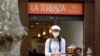 Una camarera con máscara protectora lleva bebidas a los clientes en una sección de asientos al aire libre de un restaurante en Ramblas, ya que algunas provincias españolas pueden aliviar las restricciones de bloqueo durante la fase uno.