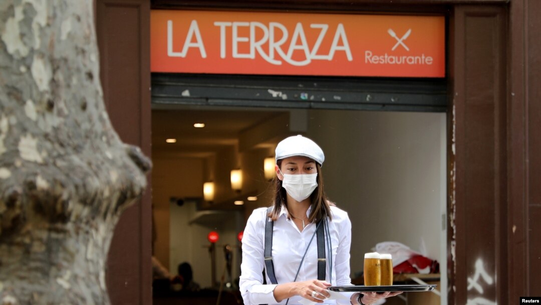 Una camarera con máscara protectora lleva bebidas a los clientes en una sección de asientos al aire libre de un restaurante en Ramblas, ya que algunas provincias españolas pueden aliviar las restricciones de bloqueo durante la fase uno.