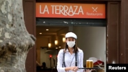 Una camarera con máscara protectora lleva bebidas a los clientes en una sección de asientos al aire libre de un restaurante en Ramblas, ya que algunas provincias españolas pueden aliviar las restricciones de bloqueo durante la fase uno.