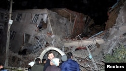 People stand outside a collapsed building after an earthquake in Elazig, Turkey, Jan. 24, 2020. 