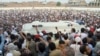 FILE - People gather around an ambulance carrying the coffin of Awami National Party (ANP) candidate Haroon Bilour, who was among those killed in a suicide attack during a July 10 election campaign meeting, in Peshawar, Pakistan, July 11, 2018.