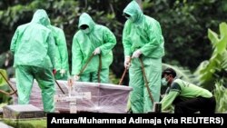 Para pekerja bersiap untuk menguburkan seorang korban yang meninggal akibat COVID-19 di area pemakaman Pondok Ranggon di Jakarta, 30 Maret 2020. (Foto: Antara/Muhammad Adimaja via Reuters)