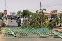 Sudanese walk past a makeshift barricade erected along a street in the capital Khartoum's twin city of Omdurman, July 1, 2019.