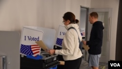 Dos votantes escanean su boleta electoral en un centro de voto anticipado en Arlington, Virginia, el 24 de octubre de 2024, en unos comicios donde el tema migratorio ha tenido protagonismo. [ARCHIVO: Tomás Guevara, VOA]. 