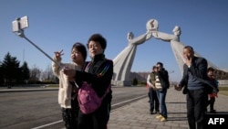 FILE - Tourists from China pose for photos before the Three Charters monument in Pyongyang, April 15, 2019. North Korea will ban foreign tourists to protect itself against a new virus, a major tour operator said Jan. 22, 2020.