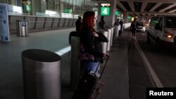 Seorang perempuan menggenakan masker menunggu di luar bandara LaGuardia di Queens, New York, 12 Maret 2021. (Foto: Shannon Stapleton/Reuters)