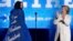 Hillary Clinton aplaude a la artista Katy Perry al subir al escenario de un mitin en Filadelfia. Su capa tiene un letrero que dice: "Apoyo a la señora presidenta".