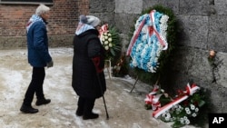 Former prisoners place candles and flowers at the Death Wall marking the 74th anniversary of the liberation of KL Auschwitz-Birkenau, in Oswiecim, Poland, Jan. 27, 2019.