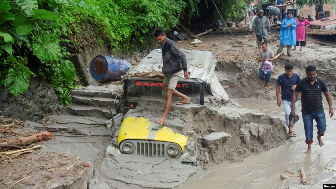 People walk along a street as a jeep is buried in the mud due to the flood at Teesta Bazaar in Kalimpong District, West Bengal, India, on Oct. 4, 2023.