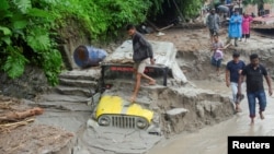 People walk along a street as a jeep is buried in the mud due to the flood at Teesta Bazaar in Kalimpong District, West Bengal, India, on Oct. 4, 2023.