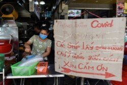 FILE - A woman sells food next to a banner reading "prevent the spread of COVID-19, take away only, please keep your distance 2 meters" amid the coronavirus outbreak in Hanoi, Vietnam, May 31, 2021.