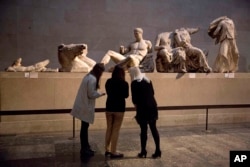 FILE - Women stand by a marble statue of a naked youth thought to represent Greek god Dionysos, center, from the east pediment of the Parthenon at the British Museum in London, on Jan. 8, 2015. (AP Photo/Matt Dunham, File)
