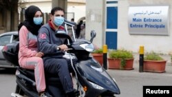 People wearing face masks ride on a motorbike outside Rafik Hariri hospital, where Lebanon's first coronavirus case is being quarantined, in Beirut, Lebanon, Feb. 21, 2020. 