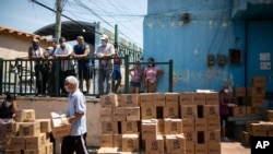 Residentes ayudan a descargar y apilar cajas de alimentos básicos proporcionados por un programa de asistencia alimentaria del gobierno en disputa conocido como CLAP, en Petare. Caracas, Venezuela. 30 de abril de 2020.