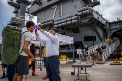 FILE - Sailors on the aircraft carrier USS Theodore Roosevelt, who have tested negative twice for COVID-19, are asymptomatic and completed their quarantine, prepare to board the clean ship, May 1, 2020. (AFP/US Navy/Nathan Carpenter/Handout)