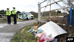 Flowers and messages of condolence for Sarah Everard are seen as police patrol near the woodland where officers found what turned out to be her remains near Ashford, southeast England, on March 12, 2021, 