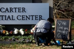 John Newberry, staf Habitat for Humanity, bersama putranya Rory Newberry (11 bulan), meletakkan helm pengaman berwarna biru untuk memberi penghormatan kepada mantan Presiden Amerika Serikat Jimmy Carter, di Atlanta, Georgia, AS, 30 Desember 2024. (Octavio Jones/REUTERS)