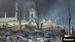 FILE - A man stands in front of a mosque as it burns in Meikhtila, Myanmar, March 21, 2013. A high-level government official in Myanmar’s Rakhine State is set on demolishing hundreds of buildings, including mosques and Islamic religious schools.