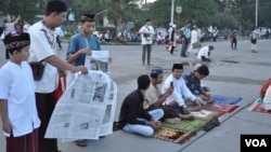 A family lays out a newspaper to be seated for morning prayer. (K. Varagur/VOA)