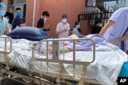 A patient on a hospital bed is pushed past a line of residents waiting to be tested at a fever clinic in Beijing, China, June 15, 2020.