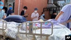 A patient on a hospital bed is pushed past a line of residents waiting to be tested at a fever clinic in Beijing, China, June 15, 2020. 