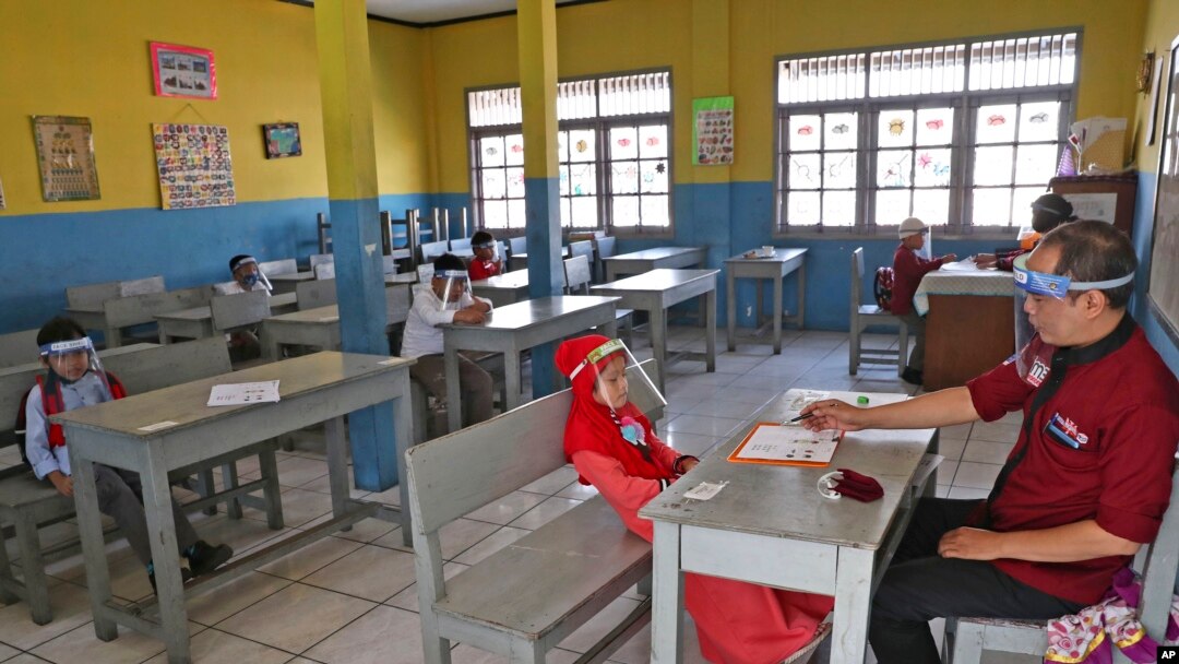 Children wearing face shield as a precaution against the new coronavirus outbreak sit spaced apart as they wait for their turn to take an admission test at Al Hidayah Islamic Elementary School in Jakarta, Indonesia, Monday, July 6, 2020. 
