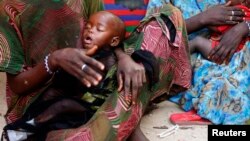 FILE - A woman holds her malnourished child in Sirlaabe IDP camp in Mogadishu, Somalia.