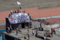 FILE - Inmates hold a sign that reads in Spanish "We want COVID-19 tests, we have the right to live"," as they gather ona roof during a prison protest at Lurigancho prison in Lima, Peru, April 28, 2020.