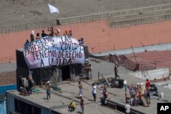 FILE - Inmates hold a sign that reads in Spanish "We want COVID-19 tests, we have the right to live"," as they gather ona roof during a prison protest at Lurigancho prison in Lima, Peru, April 28, 2020.