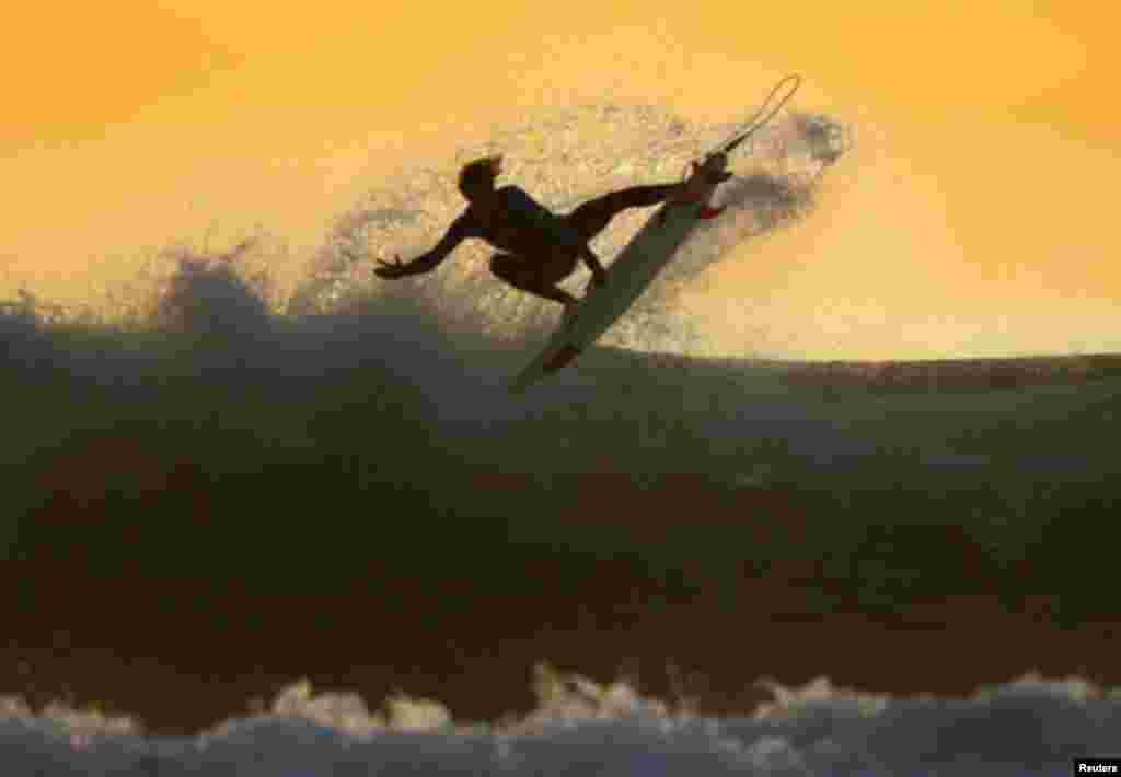 A young surfer sails his board off a wave as large swells hit the California coastline at dusk in Cardiff , California January 5, 2012. REUTERS/Mike Blake (UNITED STATES - Tags: SOCIETY ENVIRONMENT)