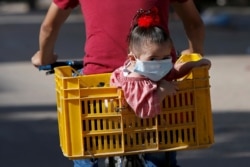 A Palestinian girl wearing a protective face mask sits in a box on the back of a bicycle amid the coronavirus disease (COVID-19) crisis, in Gaza City.