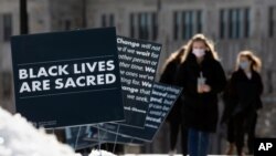 Students walk past Black History Month posters on the Boston College campus, Feb. 17, 2021, in Boston. Harassment by white male students targeting Black and Latina women housed in a Boston College dormitory has revived concerns about racism on campus.