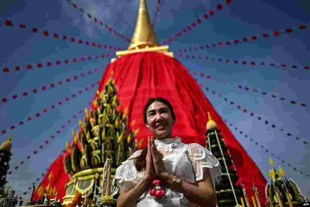 A woman poses in front of the Phra Borom Banphot Chedi, or stupa, draped in red cloth atop the Wat Saket Buddhist temple in Bangkok on Nov. 8, 2024, to mark the start of a 10-day annual fair ahead of Thailand's Loy Krathong festival. 