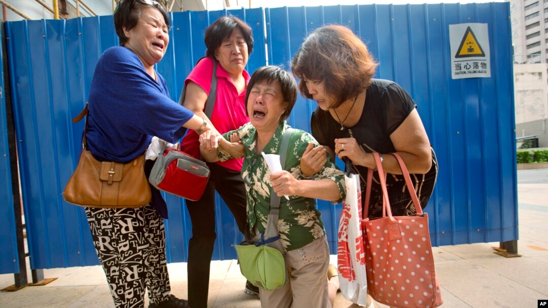 Bao Lanfang, second from right, whose daughter-in-law, son and granddaughter were aboard Malaysia Airlines Flight 370, kneels in grief while speaking to journalists outside the company's offices in Beijing, Aug. 6, 2015. 