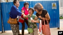 Bao Lanfang, second from right, whose daughter-in-law, son and granddaughter were aboard Malaysia Airlines Flight 370, kneels in grief while speaking to journalists outside the company's offices in Beijing, Aug. 6, 2015. 