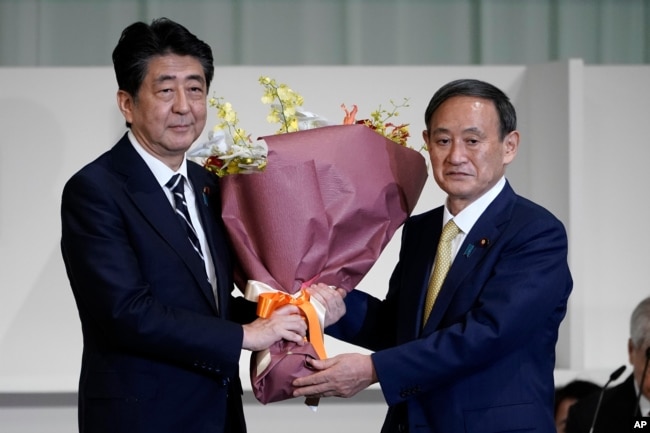 Perdana Menteri Jepang Shinzo Abe, kiri, menerima bunga dari Kepala Sekretaris Kabinet Yoshihide Suga setelah Suga terpilih sebagai ketua baru partai penguasa Jepang pada pemilihan kepemimpinan Partai Demokrat Liberal (LDP) Senin, 14 September 2020. (Foto: AP)