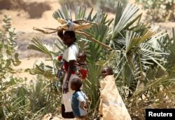 FILE - An internally displaced Sudanese woman carries her child and firewood as she walks alongside her other children within the Kalma camp for internally displaced persons (IDPs) in Darfur, April 25, 2019.