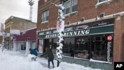 Jake Olson, left, and Mackenzie Weinberger shovel snow outside of a store in downtown Fargo, N.D., Dec. 30, 2019, following a blizzard that dropped over a foot of snow in the area and closed streets, highways and many businesses.