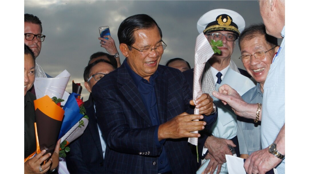 Cambodia's Prime Minister Hun Sen, center, gives a flower to a passenger from the Westerdam at the port of Sihanoukville, Cambodia, Feb. 14, 2020. Hundreds of cruise ship passengers cheered as they finally disembarked and were welcomed to Cambodia.