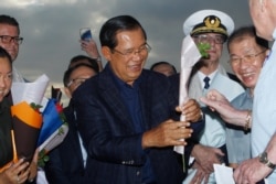 Cambodia's Prime Minister Hun Sen, center, gives a flower to a passenger from the Westerdam at the port of Sihanoukville, Cambodia, Feb. 14, 2020. Hundreds of cruise ship passengers cheered as they finally disembarked and were welcomed to Cambodia.