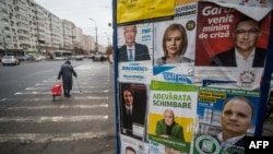 FILE - People pass by a billboard displaying posters for various candidates in the parliamentary elections, in Bucharest, Dec. 3, 2020.