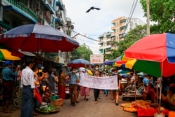 FILE - Anti-coup protesters hold signs that read "We Support NUG," which stands for National Unity Government, as they march on a street where vendors sell fresh products, April 17, 2021 in Yangon, Myanmar.